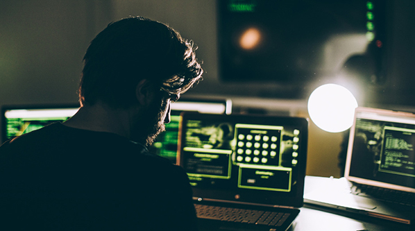 man in the dark at computer monitors